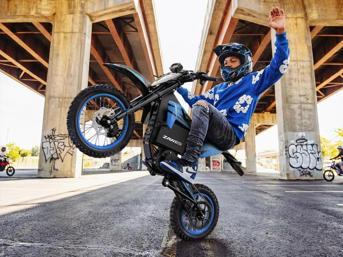 Rider in blue popping a wheelie on a ZAWES electric dirt bike under a highway overpass